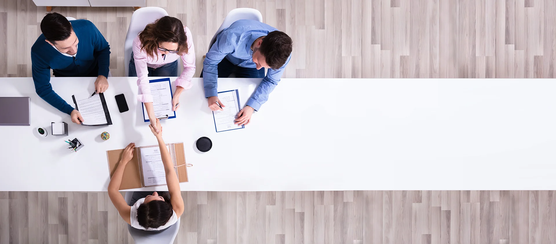 Overhead view of three interviewers welcoming a new recruit with a handshake