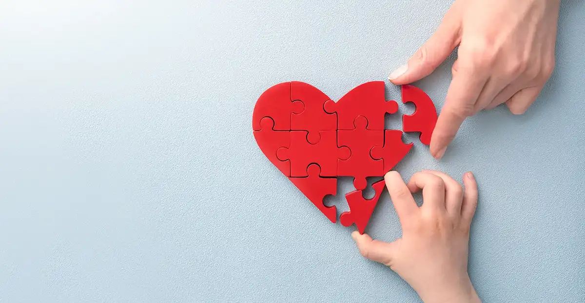 One adult and one child hand putting together a heart-shaped puzzle
