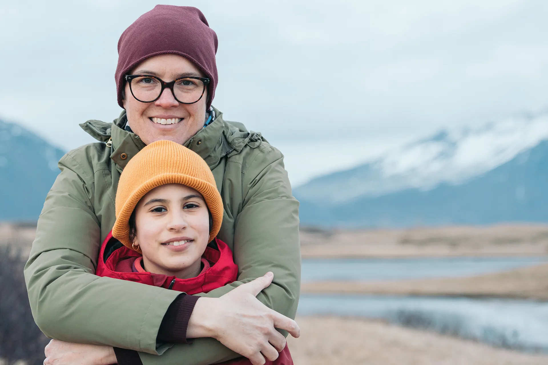 Mother hugging her smiling teenage daughter next to mountains