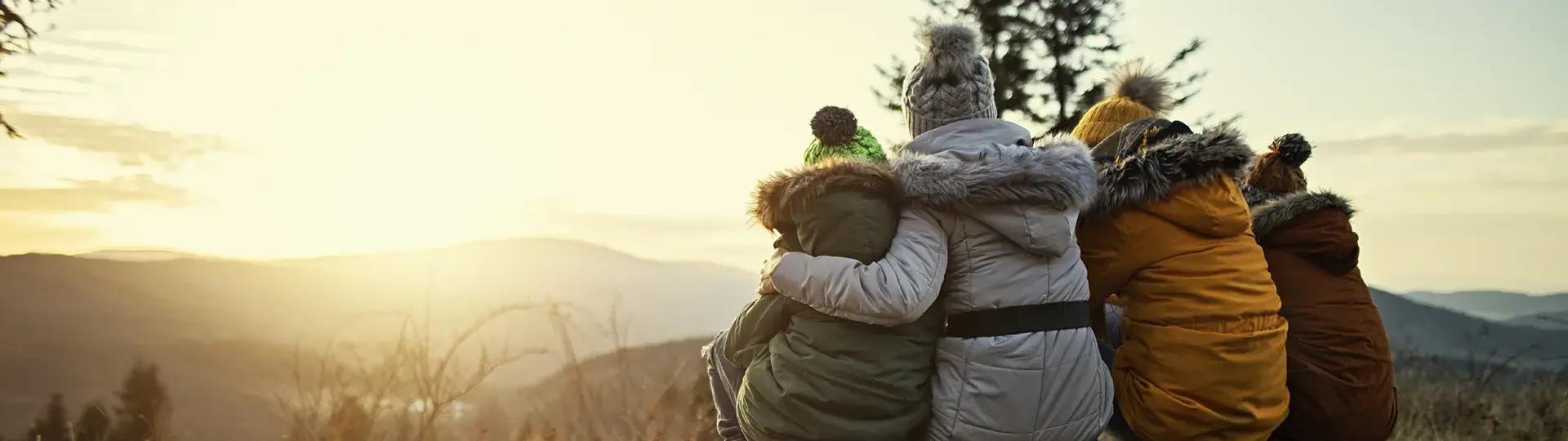 Family in winter coats, sitting on a log, watching the sunset