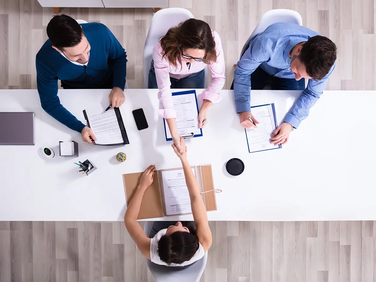Overhead view of three interviewers welcoming a new recruit with a handshake