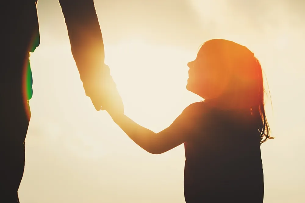 Girl holding the hand of an adult in silhouette