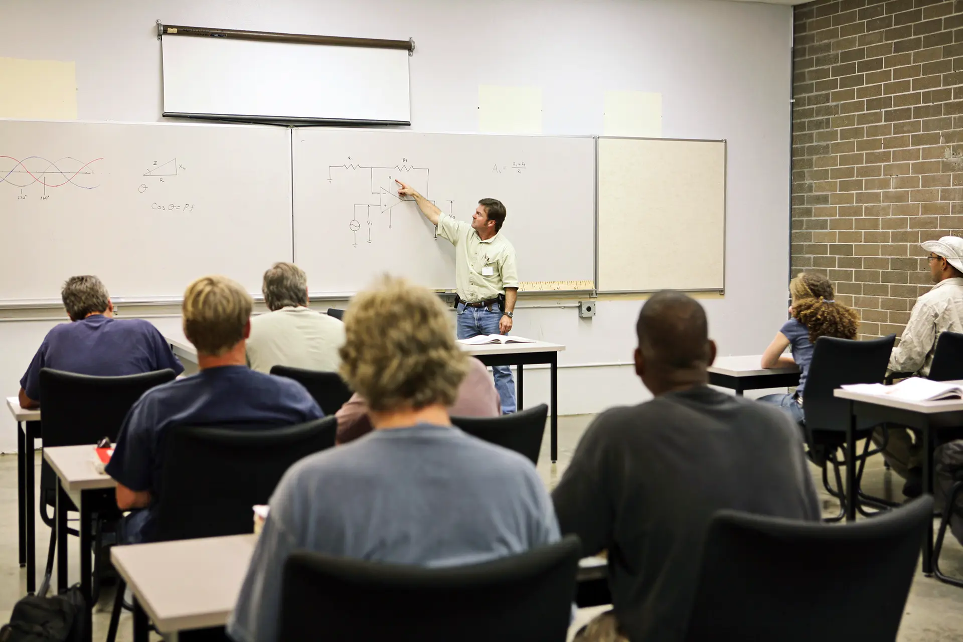 Teacher at the front of a classroom, pointing at an electrical diagram on the whiteboard