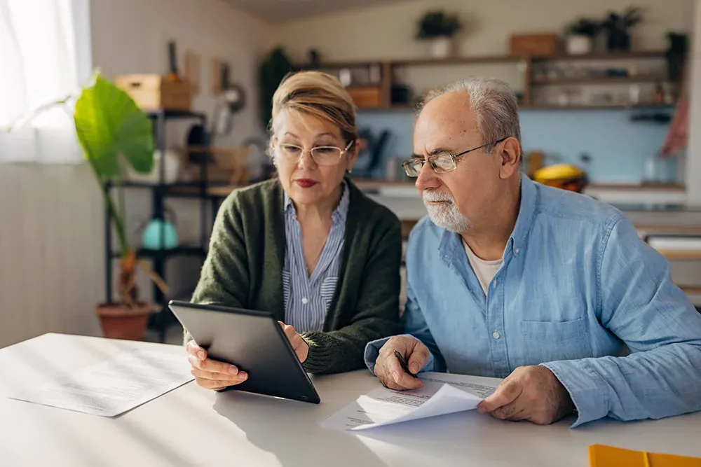 Senior couple with paperwork, looking at a tablet
