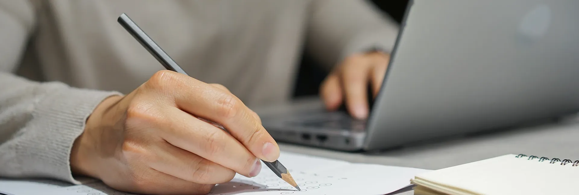 Person taking a test with a laptop, pencil and paper