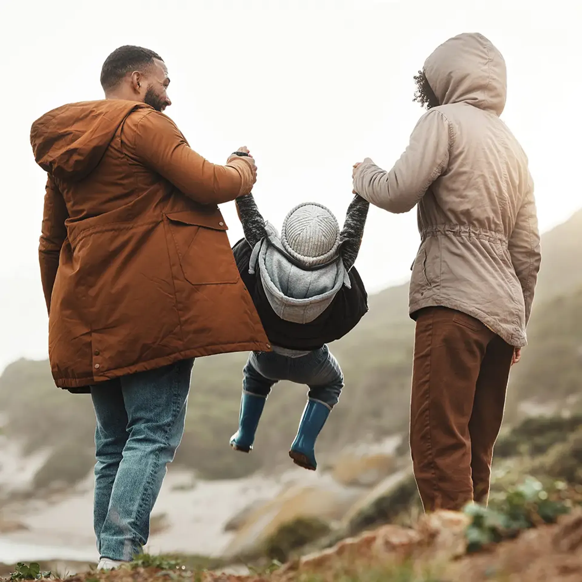 Two parents outside, swinging child by his arms