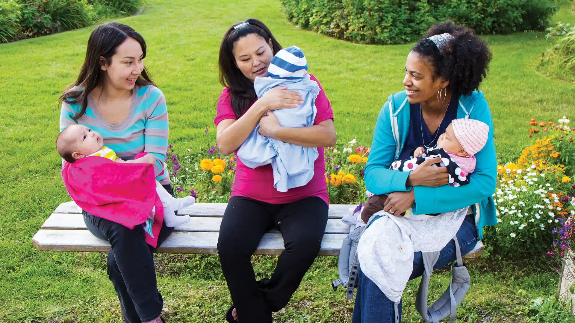 Three mothers holding their babies on a park bench