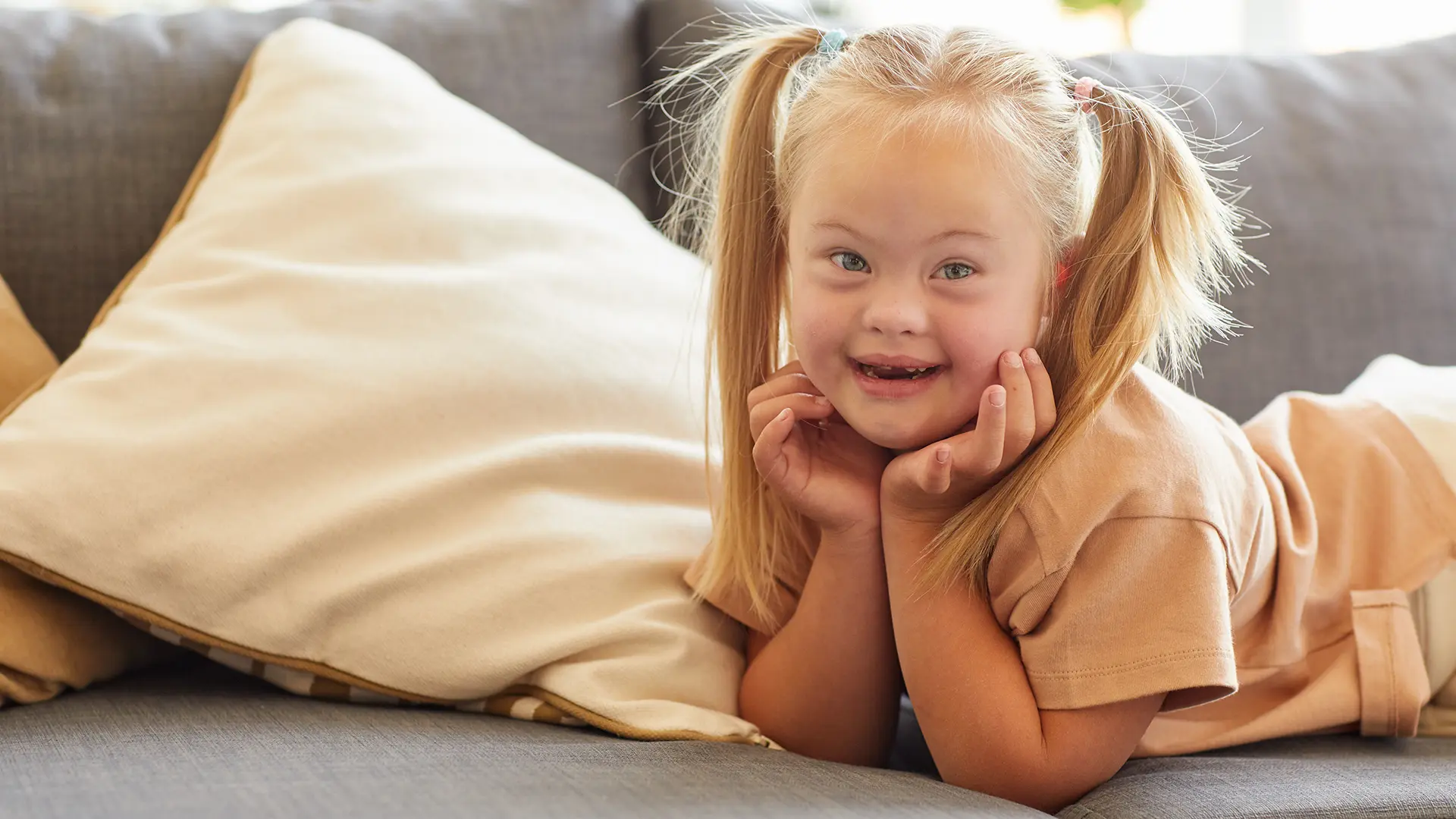 Cute girl with down syndrome smiling happily at camera while lying on sofa