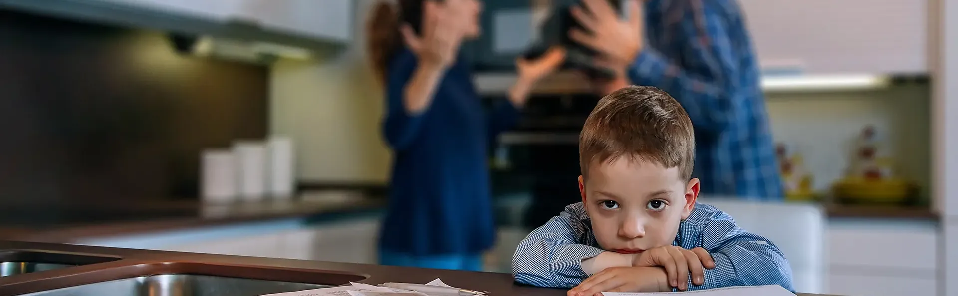 Sad boy looking at camera while his parents argue in the kitchen 