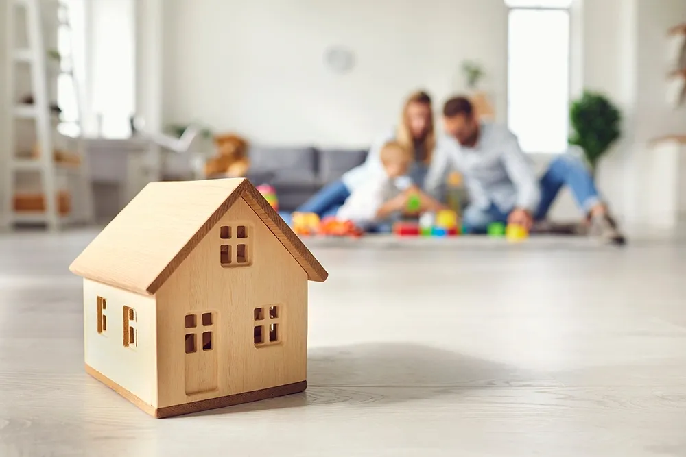 Little wooden house on floor of cozy room with family playing in background 