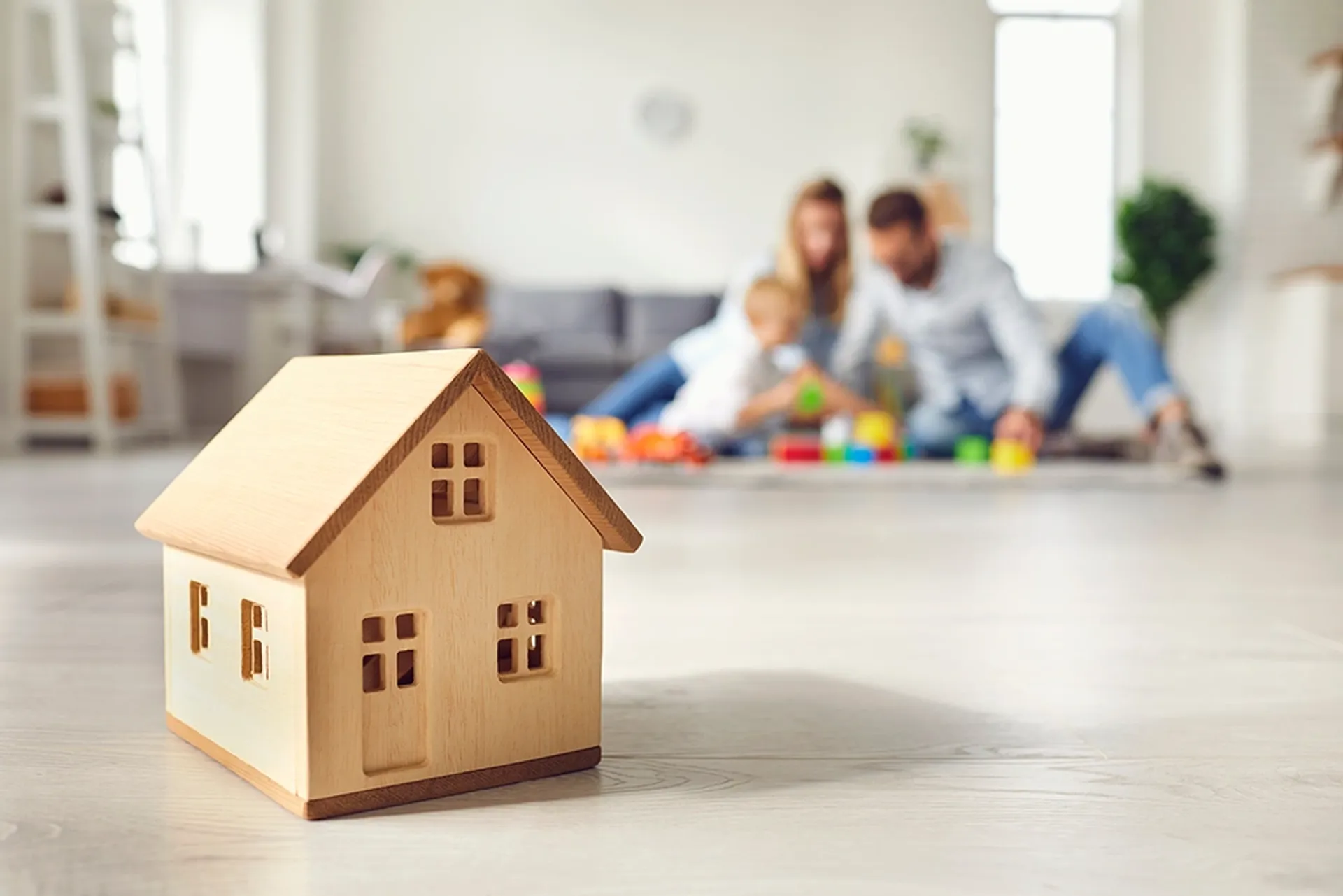 Little wooden house on floor of cozy room with family playing in background 