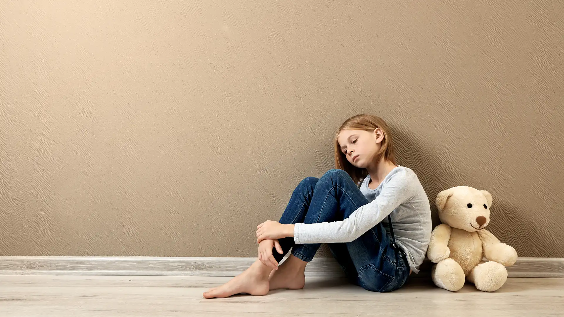 Sad girl leaning against a wall with her teddy bear