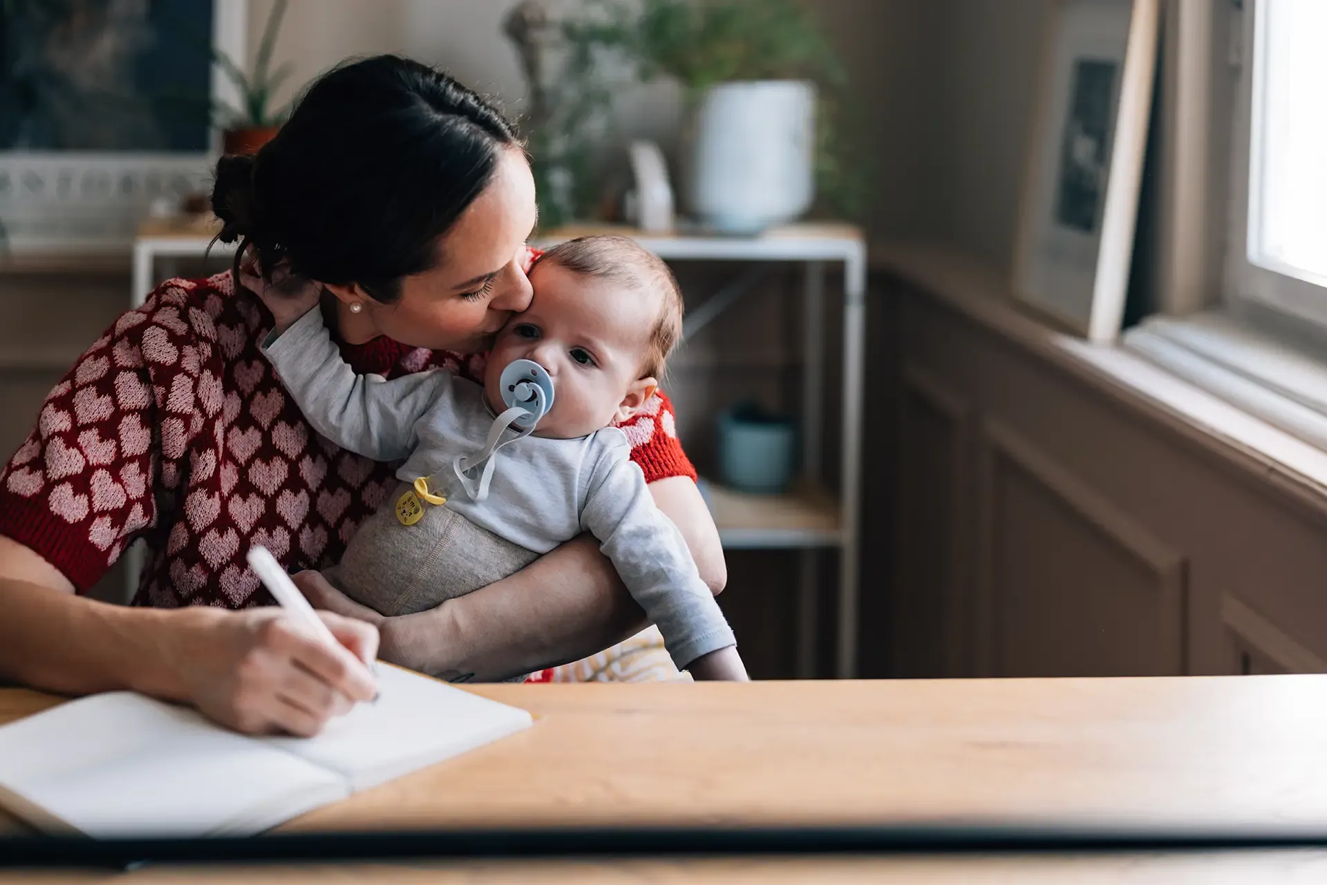 Woman kissing baby while writing in a notebook