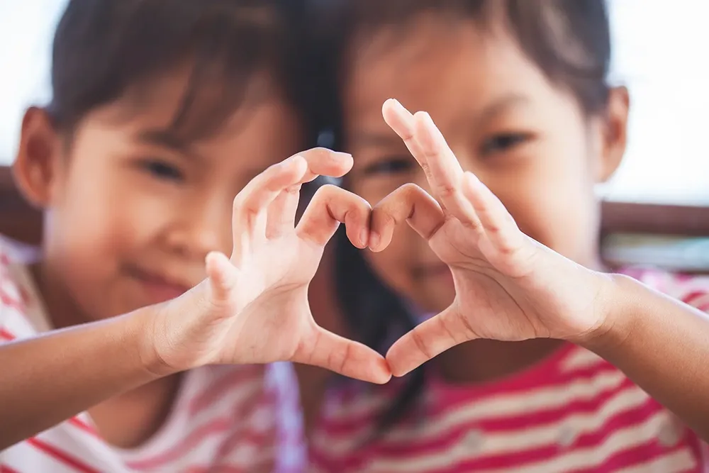 Two children making a heart shape with their hands