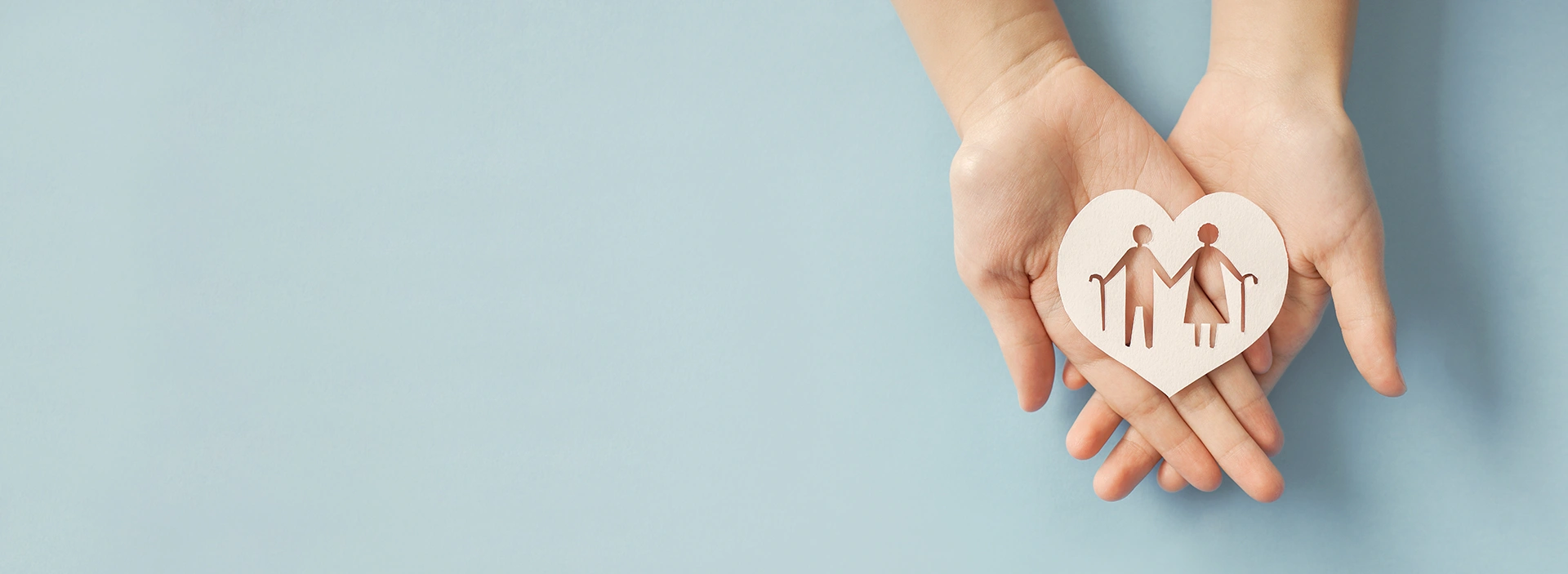 Hands supporting paper heart with elderly silhouettes cut out