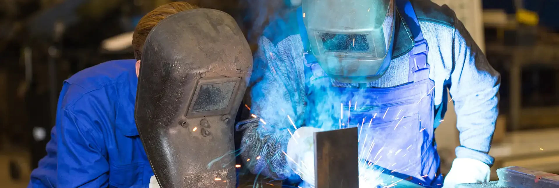 Student observing teacher welding metal