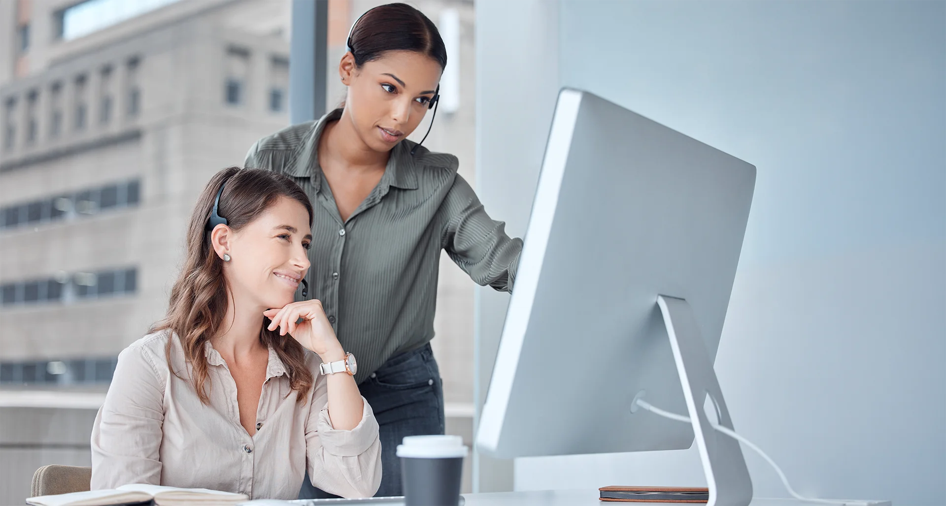 Two women in a corporate setting, one showing the other something on a computer monitor