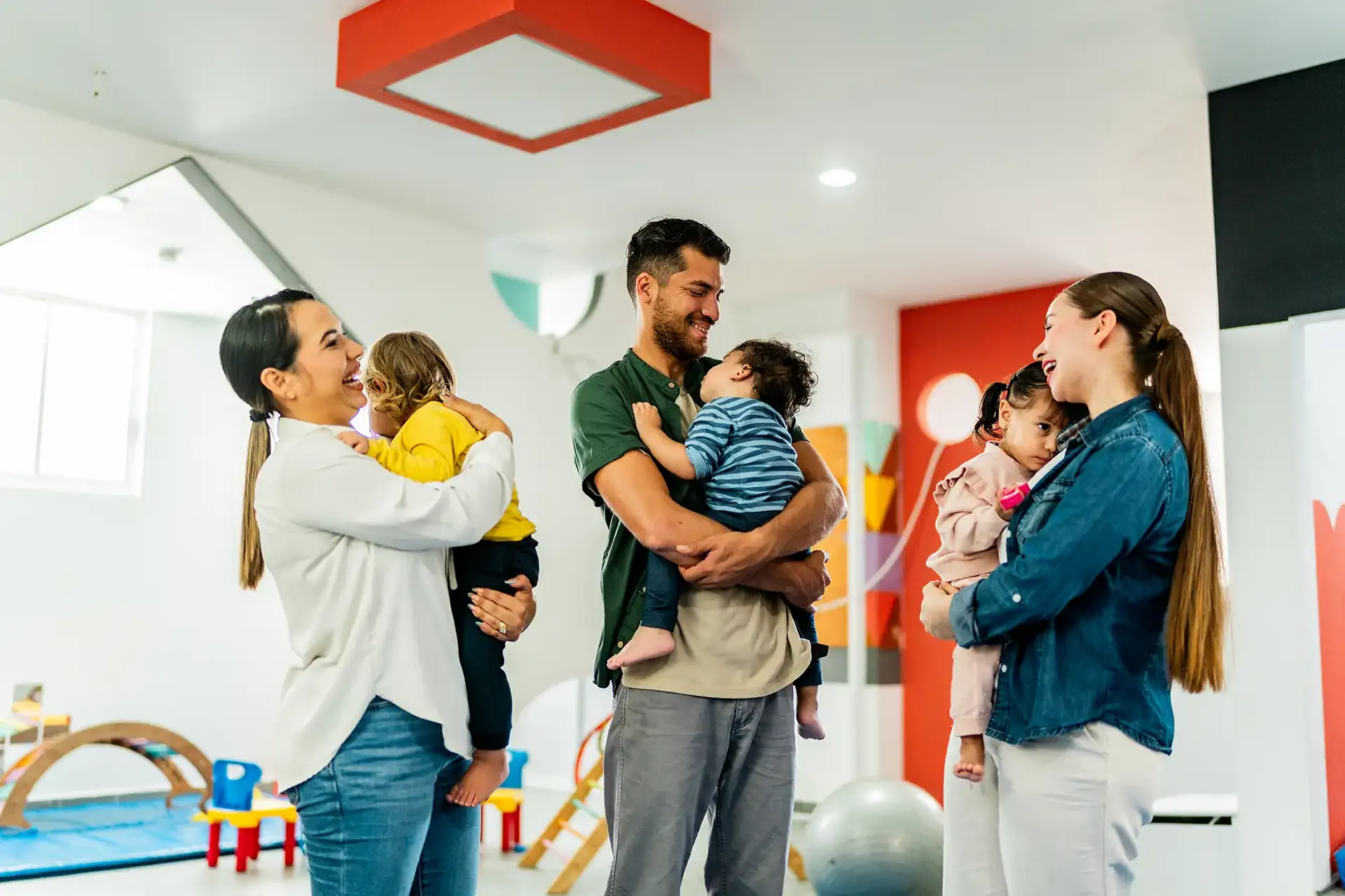 Three adults laughing holding their toddlers in a playroom