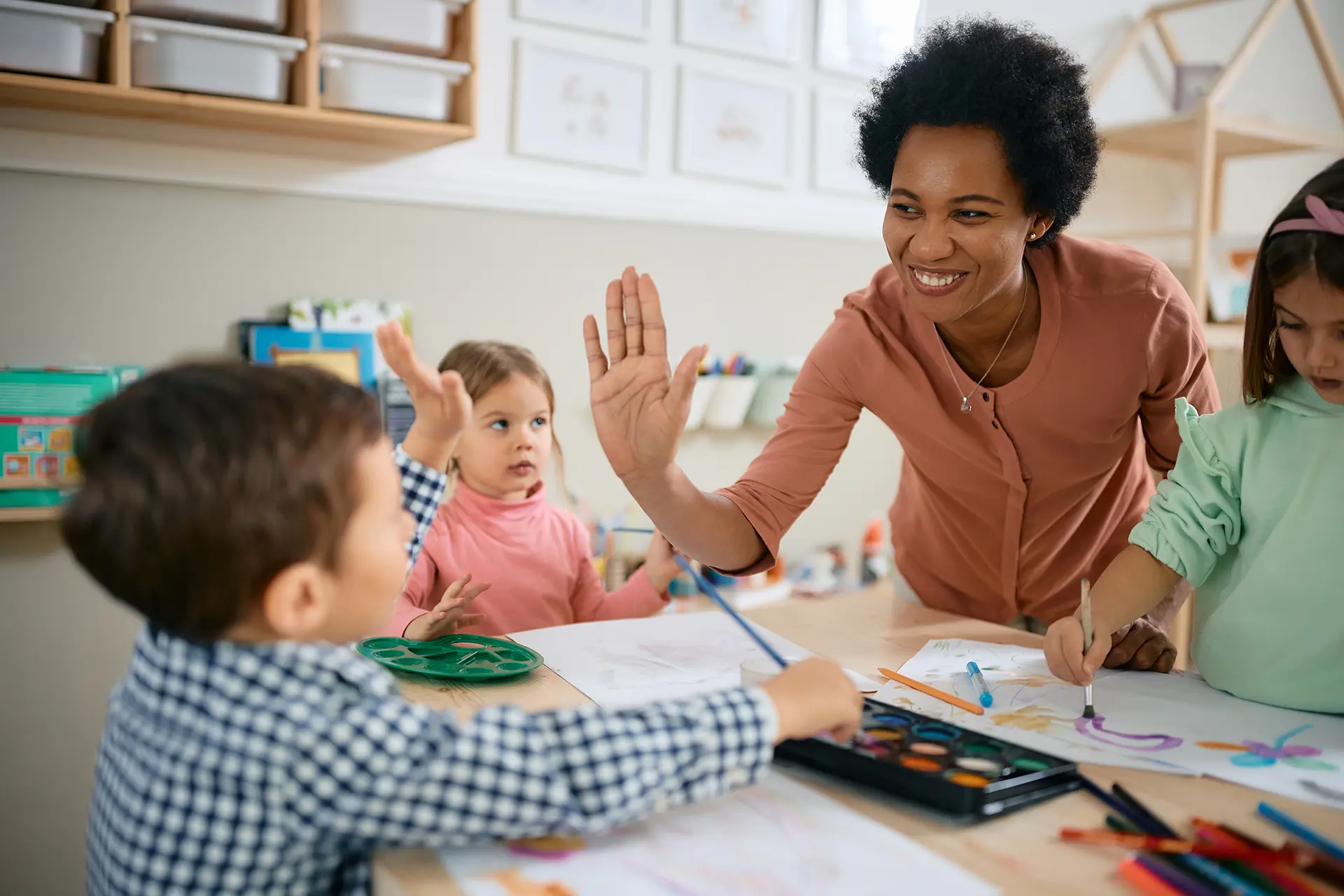 Happy African American teacher and small boy give high-five during art class at kindergarten