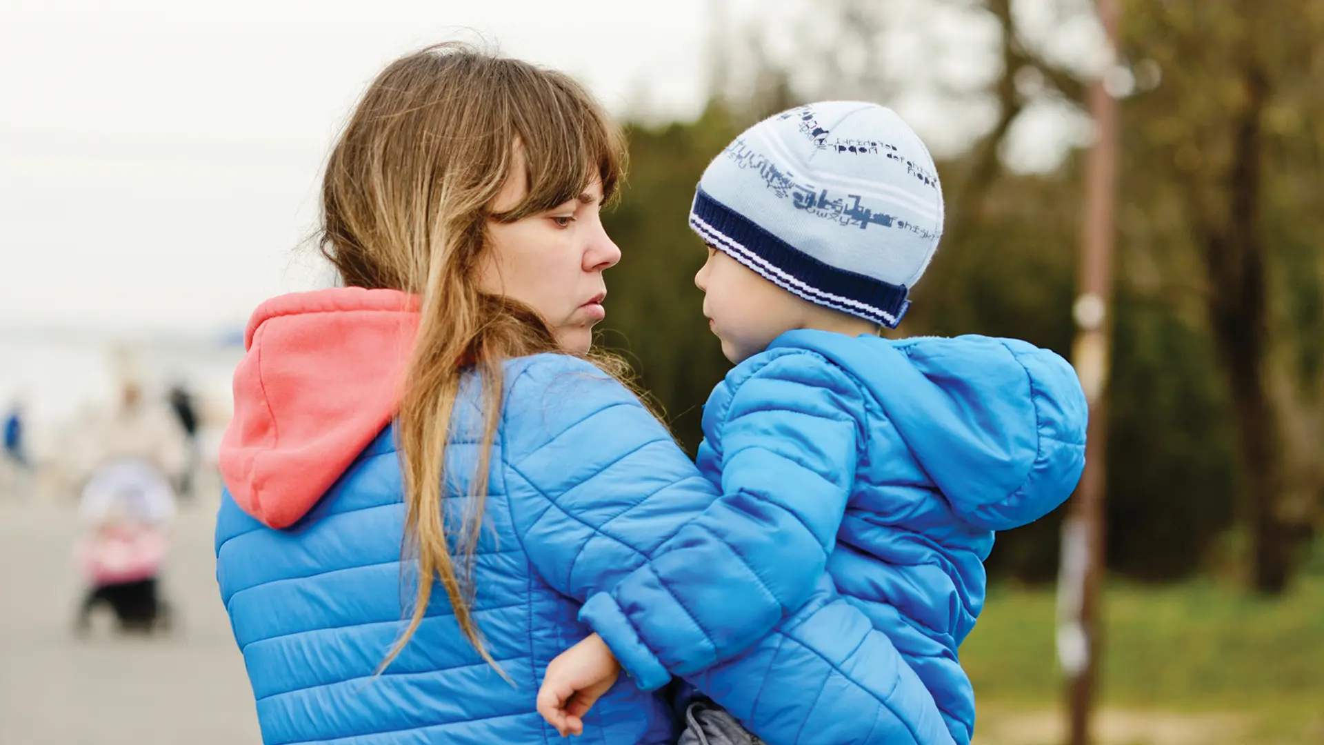 Mother holding child, both in blue coats