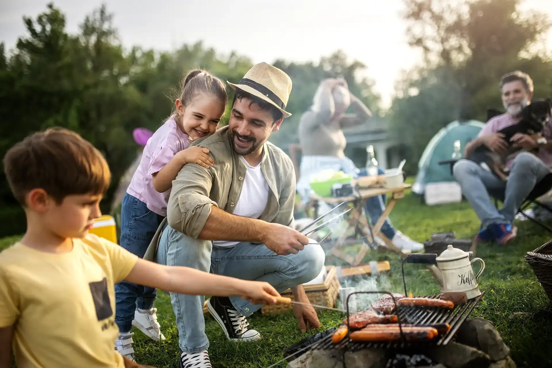 Family cooking hotdogs on a grill outdoors