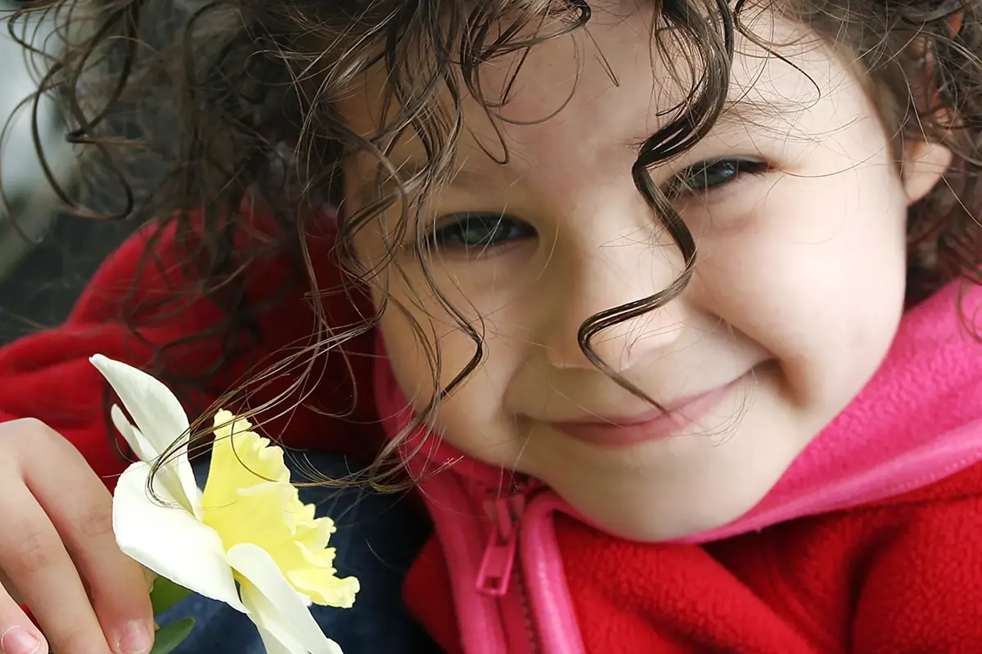 Closeup of smiling girl with curly hair, holding flower