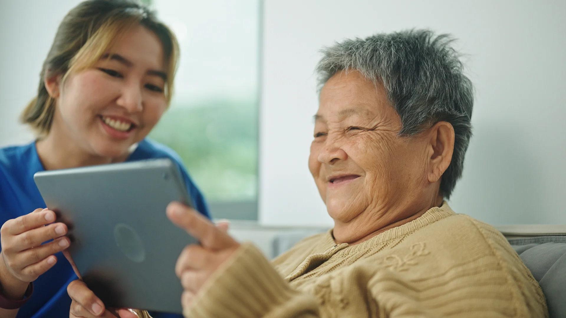 Young health care worker helping elderly woman with tablet computer