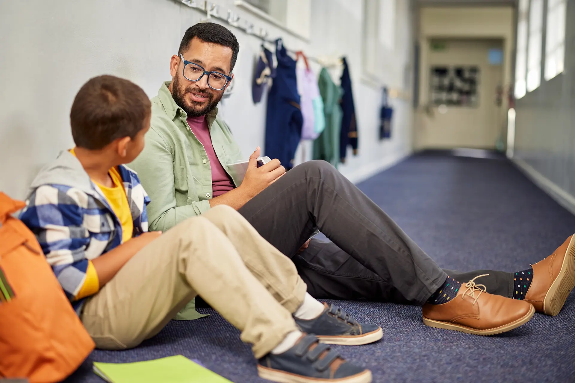 Teacher talking to young student, sitting on the floor in the hallway
