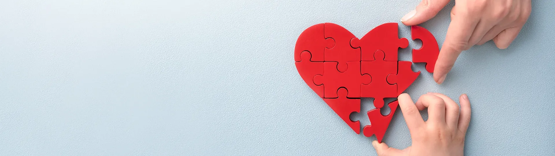 One adult and one child hand putting together a heart-shaped puzzle