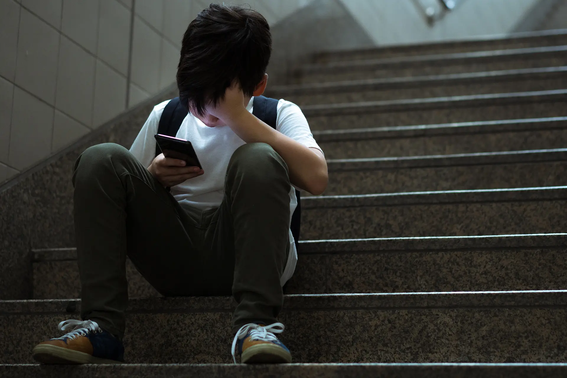 Boy sitting on stairs, face illuminated by his phone