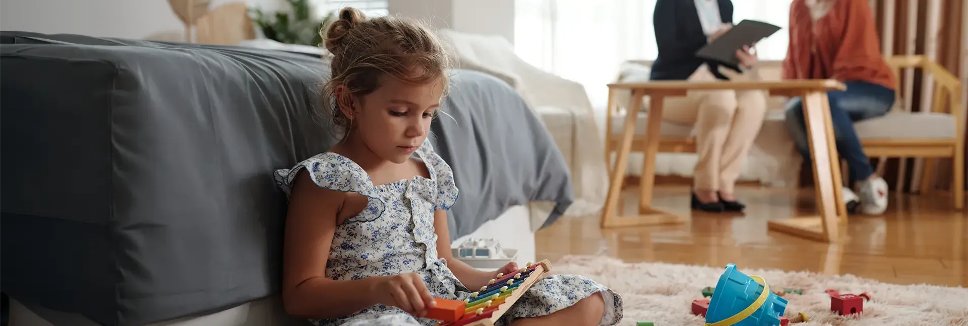 Little girl sitting playing with toys while her mom talks to a social worker 