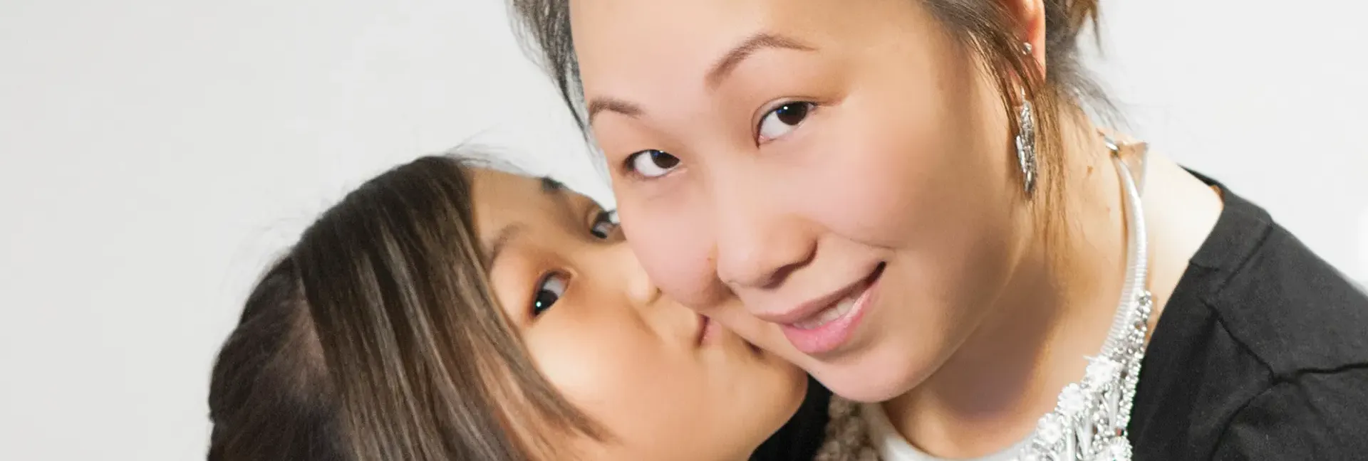 Daughter kissing smiling mom on the cheek