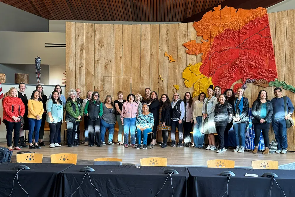 Tribal State Collaboration Group members posing for a photo in front of a carved map of Alaska