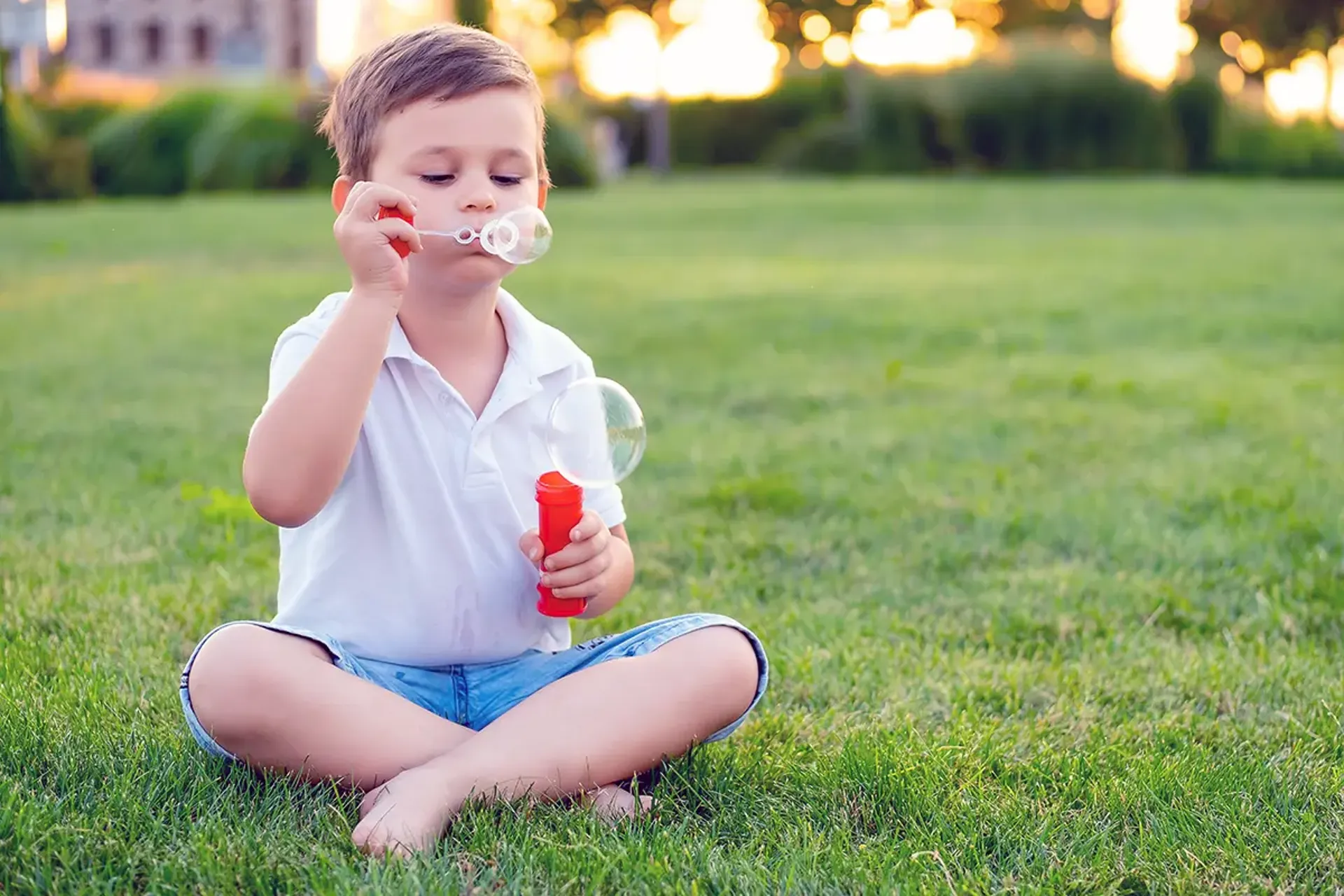 Boy sitting cross-legged on the grass, blowing bubbles