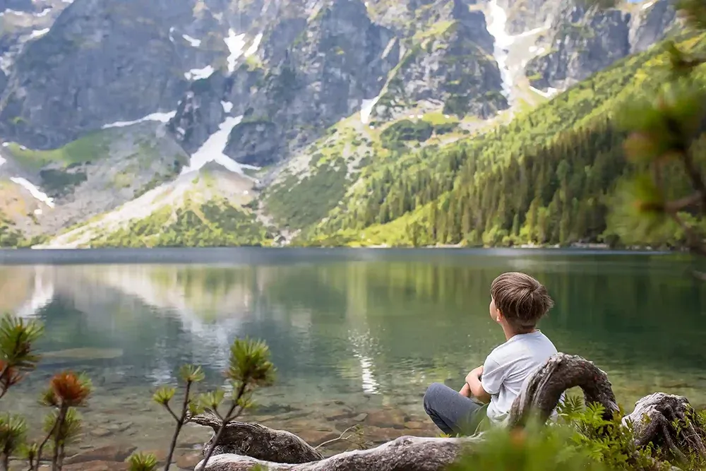 Child sitting, gazing out at an alpine lake