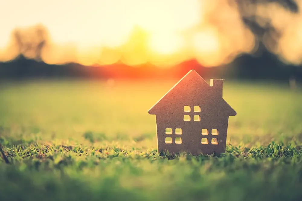Small model home on green grass with sunlit abstract background.