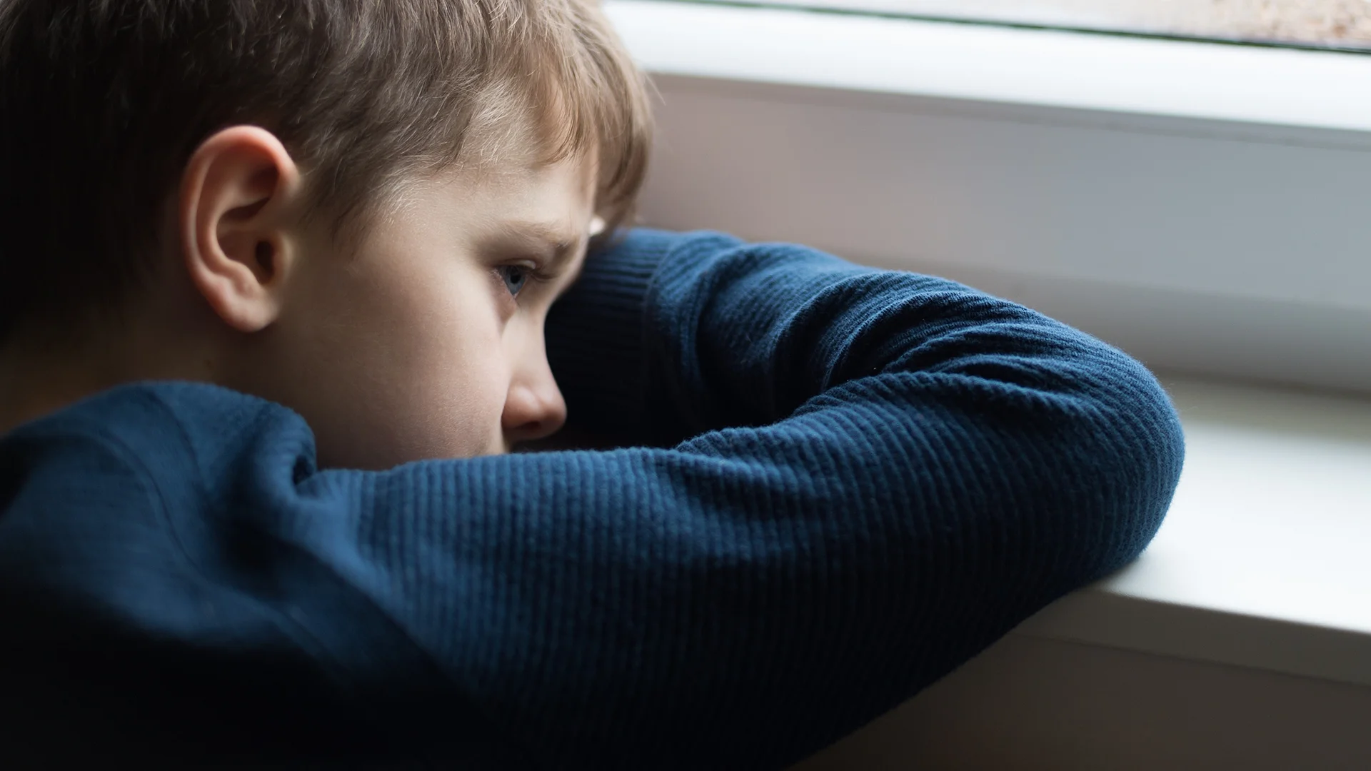 Sad boy resting head on windowsill