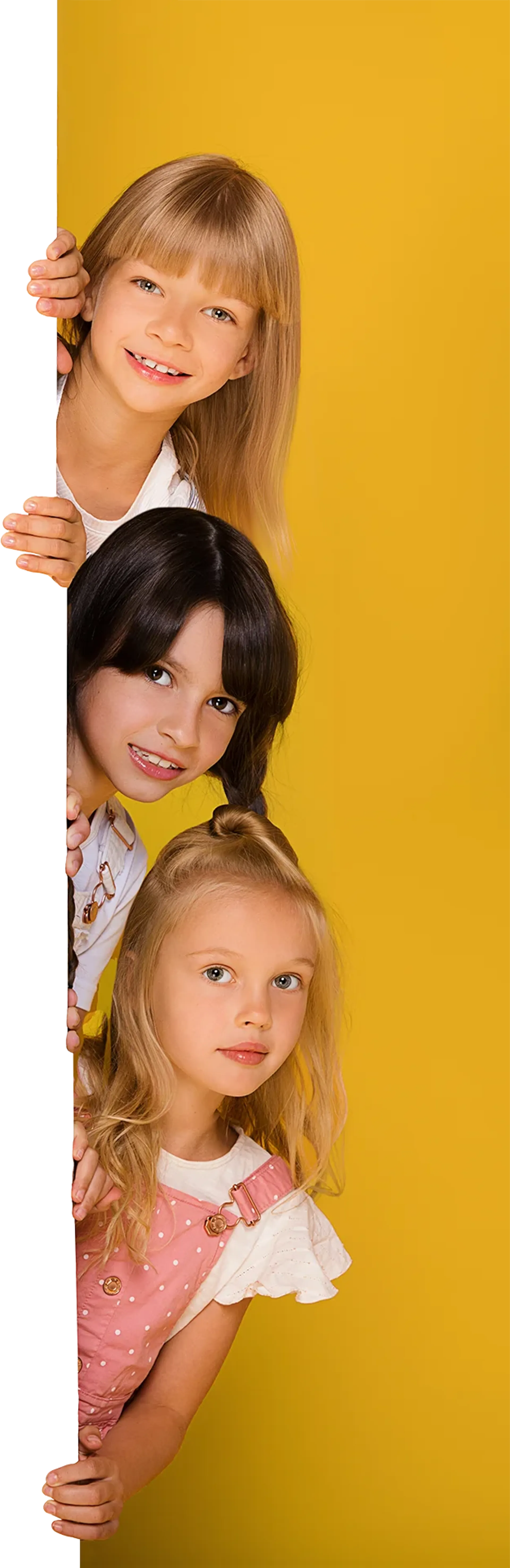 Three girls peering out from behind a wall