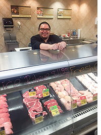 A man smiles behind a meat counter